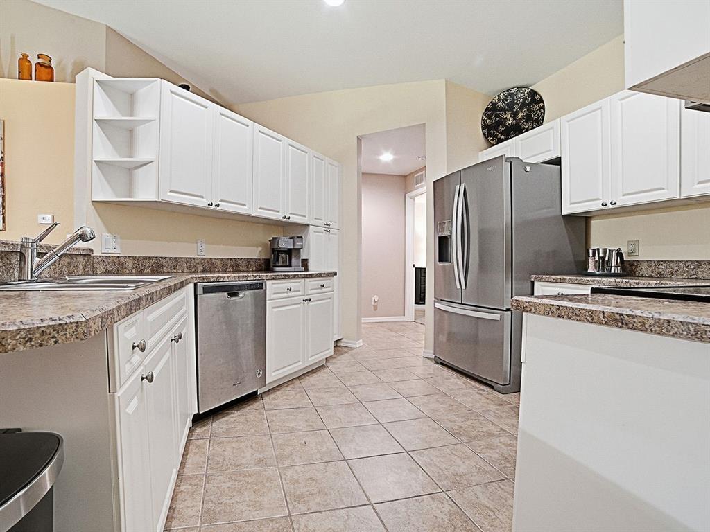 A kitchen features white cabinets, granite countertops, stainless steel appliances, and beige tile flooring — 5408 ADMIRAL WAY UNIT 11-202, OXFORD, FL