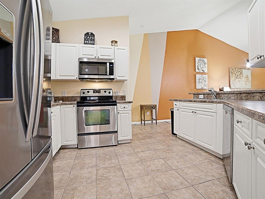 A kitchen with white cabinets, stainless steel appliances, granite countertops, and a multi-colored accent wall — 5408 ADMIRAL WAY UNIT 11-202, OXFORD, FL