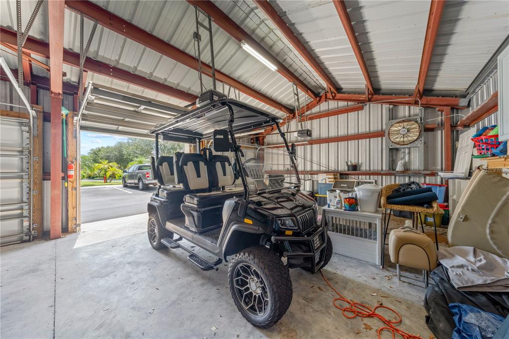 A black golf cart is parked inside a metal-framed garage with a concrete floor — 13570 MYSTIC DRIVE UNIT 102, SEBASTIAN, FL