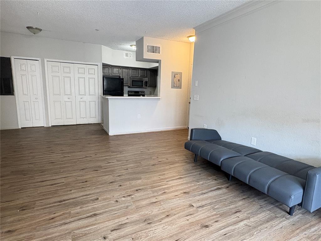 An open-concept living area features wood-look flooring, a grey futon, and a kitchen with dark cabinets — 8301 ELM PARK DRIVE UNIT 625, ORLANDO, FL