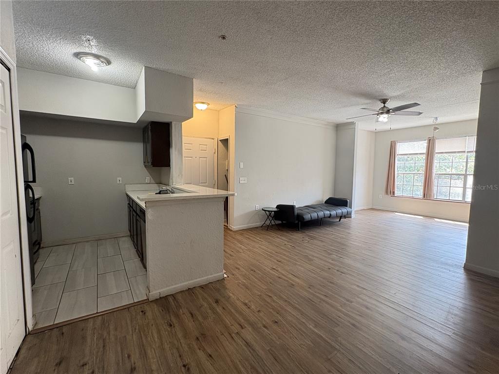 An open-concept living area features wood-look flooring, a kitchen with a breakfast bar, and windows — 8301 ELM PARK DRIVE UNIT 625, ORLANDO, FL