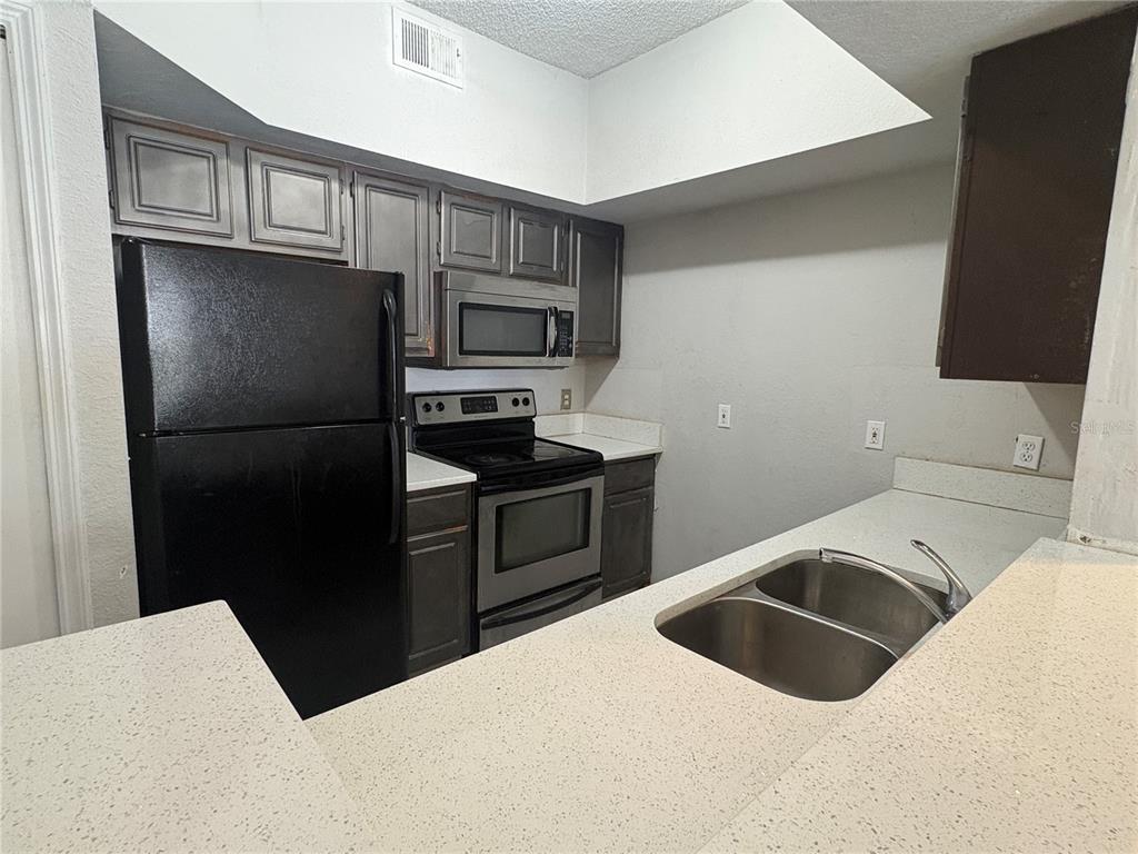 A kitchen features dark cabinets, black appliances, a double sink, and light-colored countertops — 8301 ELM PARK DRIVE UNIT 625, ORLANDO, FL