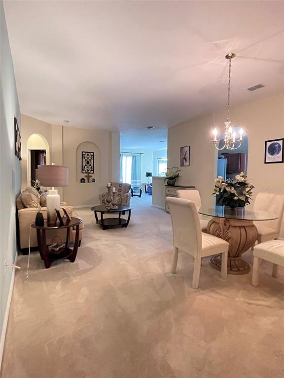 A living and dining area features beige carpeting, neutral walls, and a chandelier over the table — 5804 DORNICH DRIVE, AUBURNDALE, FL