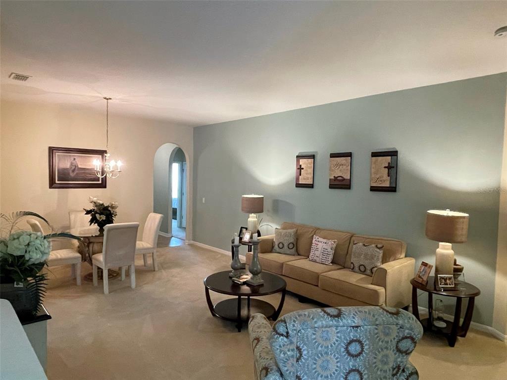 A living room and dining area feature beige carpet, a tan sofa, and light blue walls — 5804 DORNICH DRIVE, AUBURNDALE, FL