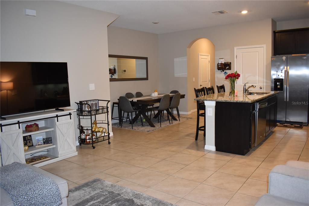 An open-concept living area features a kitchen island, dining table, and television console — 6572 SERENITY FALL LANE, SARASOTA, FL