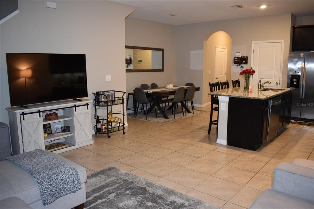 An open-concept living area features a television console, dining table, and kitchen island — 6572 SERENITY FALL LANE, SARASOTA, FL
