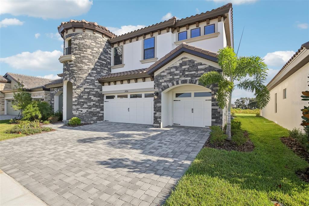 A two-story house with a stone turret, white garage doors, and a paved driveway — 14930 RIDER PASS DRIVE, LITHIA, FL