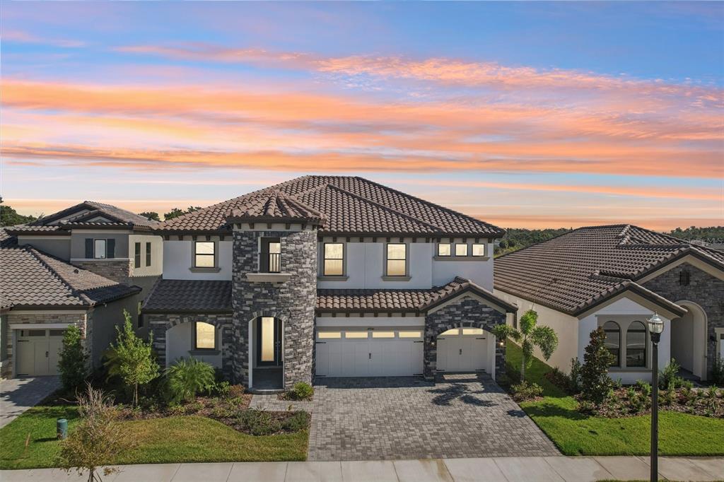 A two-story house with a stone facade, tile roof, and a paved driveway at sunset — 14930 RIDER PASS DRIVE, LITHIA, FL