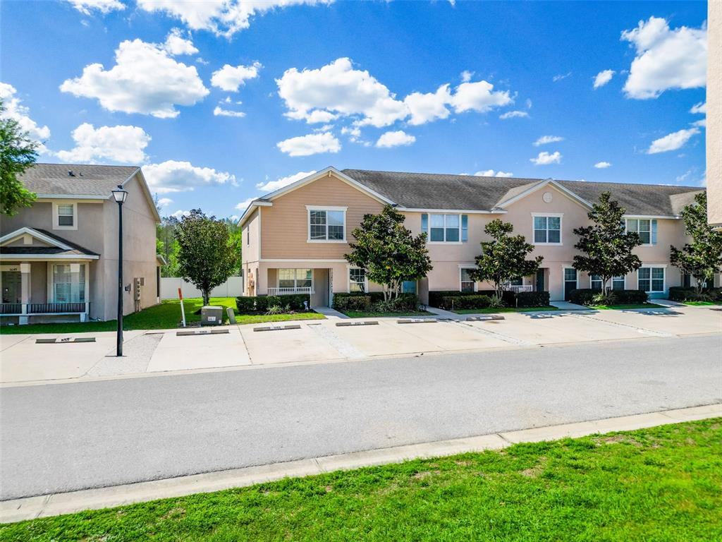 A row of tan two-story townhomes with parking spaces in front under a blue sky — 5101 CHIPOTLE LANE, WESLEY CHAPEL, FL