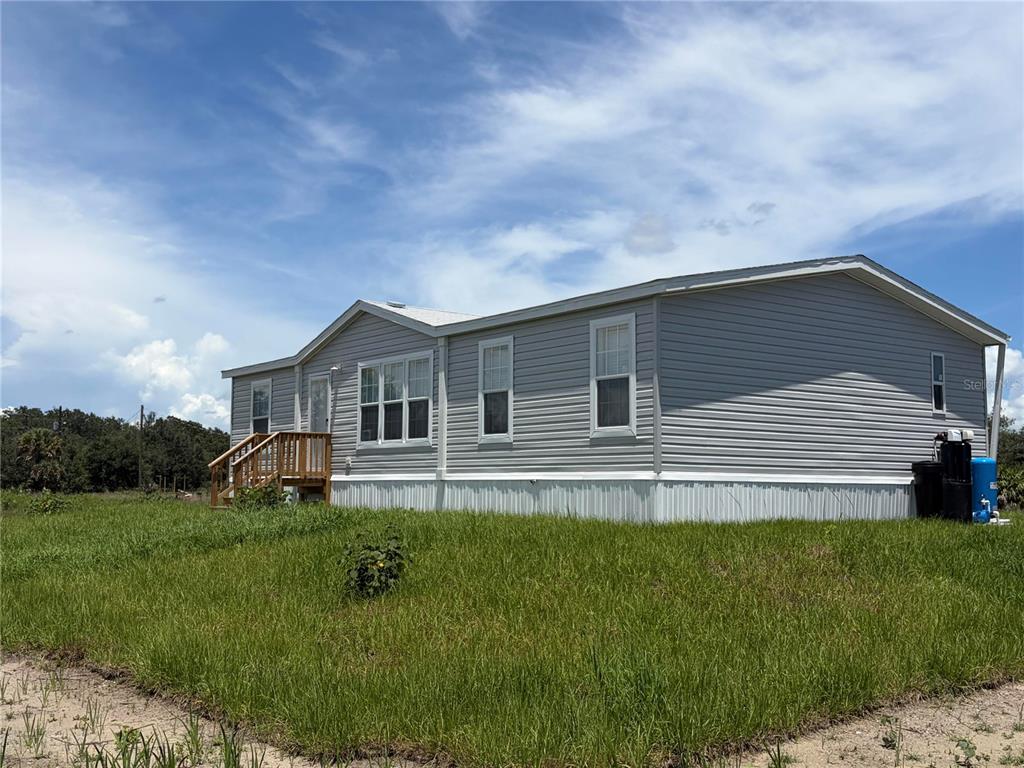 A light gray manufactured home with a wooden porch sits on a grassy lot — 19983 NW 242ND STREET, OKEECHOBEE, FL