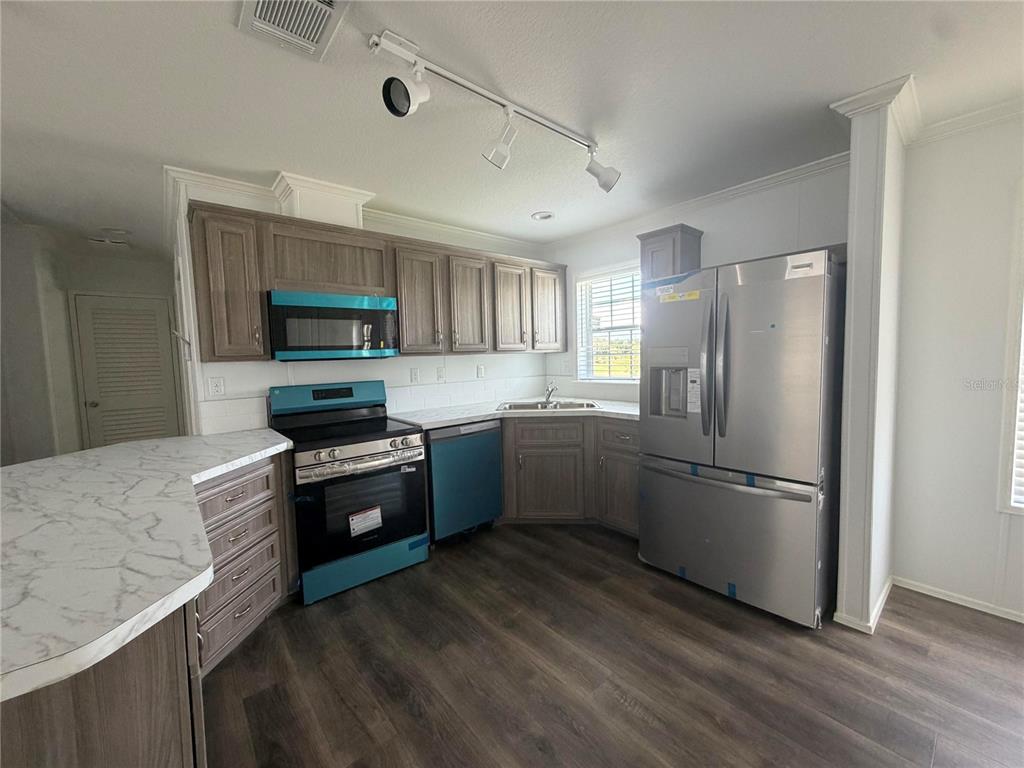 A kitchen features wood-toned cabinets, stainless steel appliances, and white marble-patterned countertops — 19983 NW 242ND STREET, OKEECHOBEE, FL