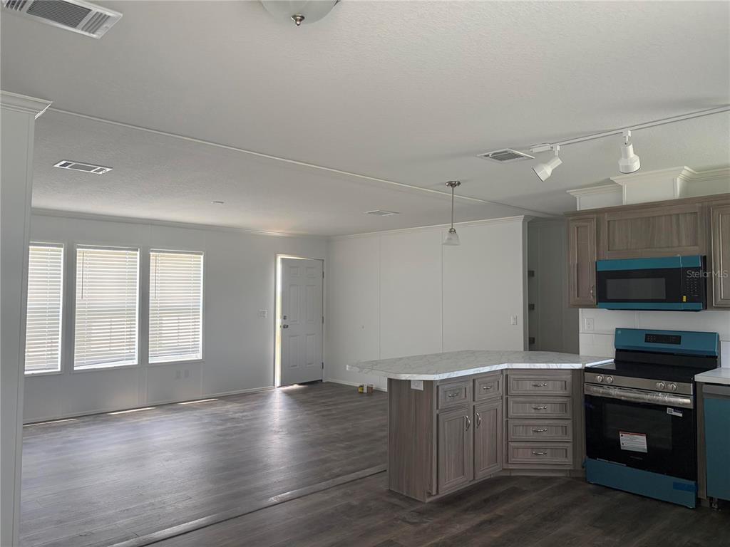 A kitchen with an island and wood-look flooring opens into a living area with windows — 19983 NW 242ND STREET, OKEECHOBEE, FL