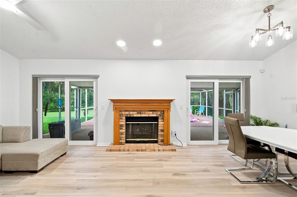 A living and dining area features a brick fireplace, light wood flooring, and sliding glass doors — 1014 HARDWOOD DRIVE, VALRICO, FL
