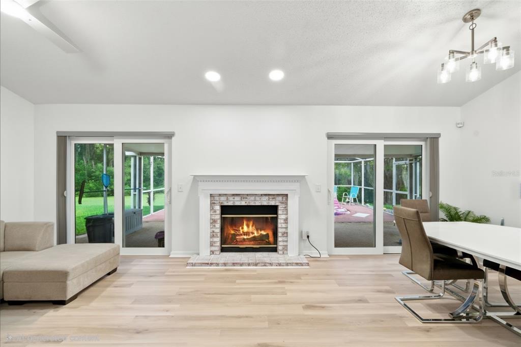 A living and dining area features a brick fireplace, light wood flooring, and sliding glass doors — 1014 HARDWOOD DRIVE, VALRICO, FL