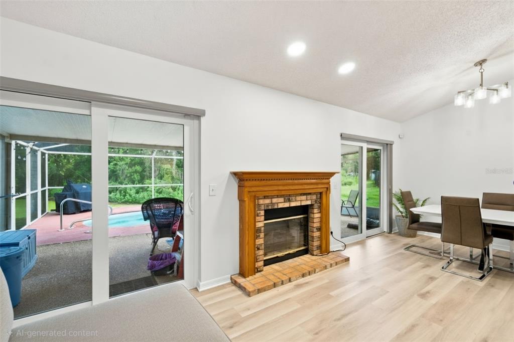 A living room with a brick fireplace, light wood flooring, and sliding glass doors to a pool — 1014 HARDWOOD DRIVE, VALRICO, FL