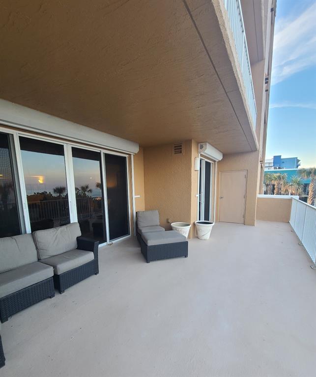 A spacious balcony features outdoor wicker furniture, potted plants, and a view of nearby buildings — 711 S ATLANTIC AVENUE Unit 202, NEW SMYRNA BEACH, FL