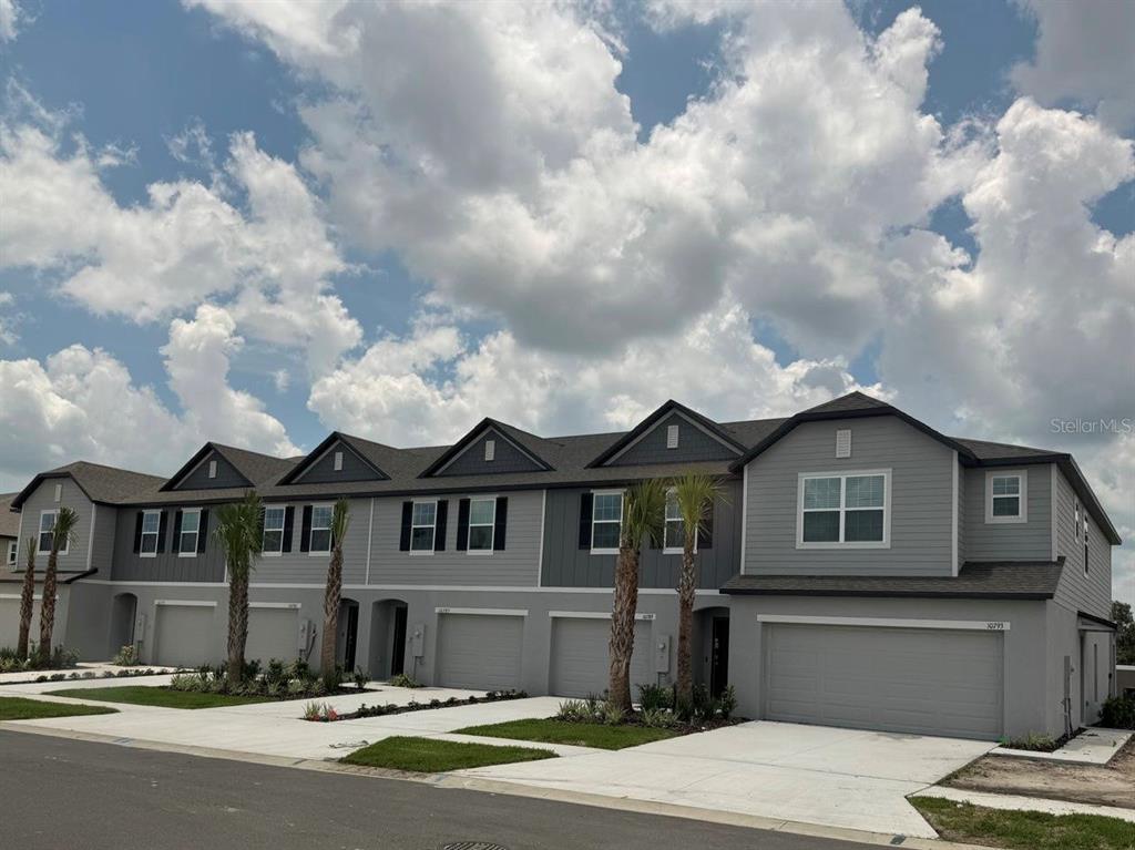 A row of multi-story townhomes with gray siding, attached garages, and palm trees in front — 10777 IRONWOOD TREE WAY, SAN ANTONIO, FL
