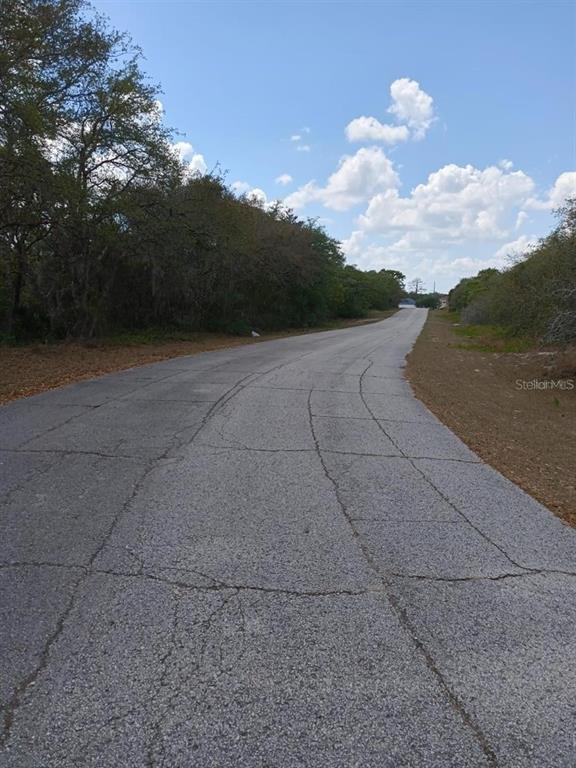 A paved road with cracks stretches forward between wooded areas under a blue sky — 429 NAPLES COURT, KISSIMMEE, FL