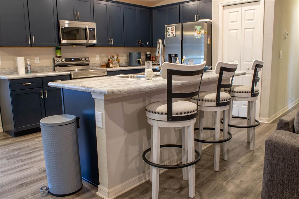 A kitchen features dark blue cabinets, a marble-look island with bar stools, and stainless appliances — 1923 GOLDEN BEAK DRIVE, EAGLE LAKE, FL