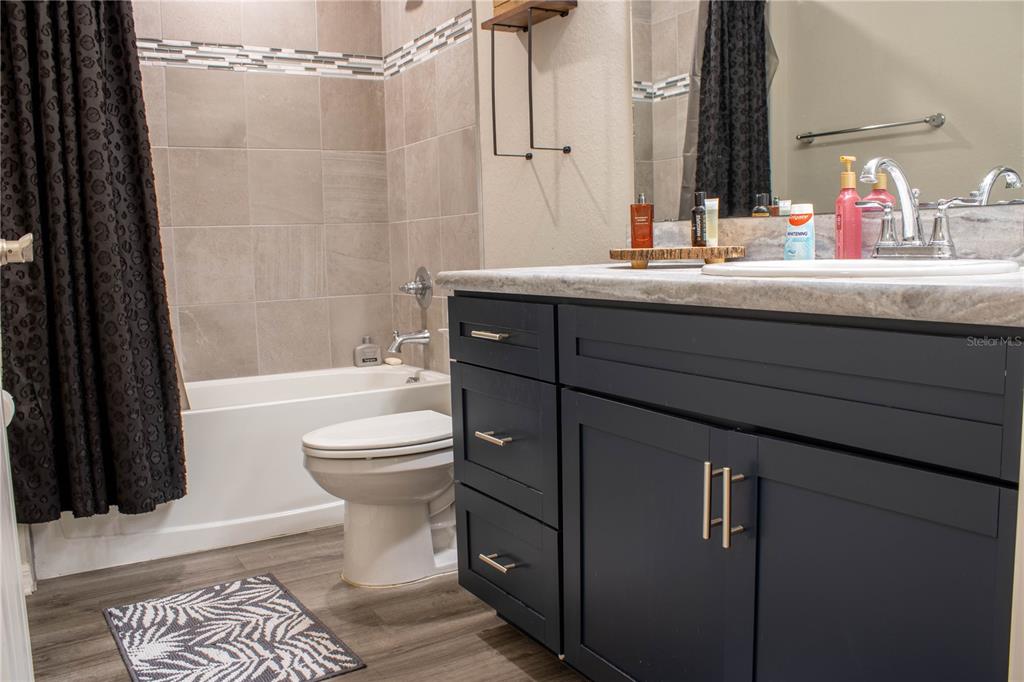 A bathroom features a dark blue vanity, a white toilet, and a tiled shower-tub combo — 1923 GOLDEN BEAK DRIVE, EAGLE LAKE, FL