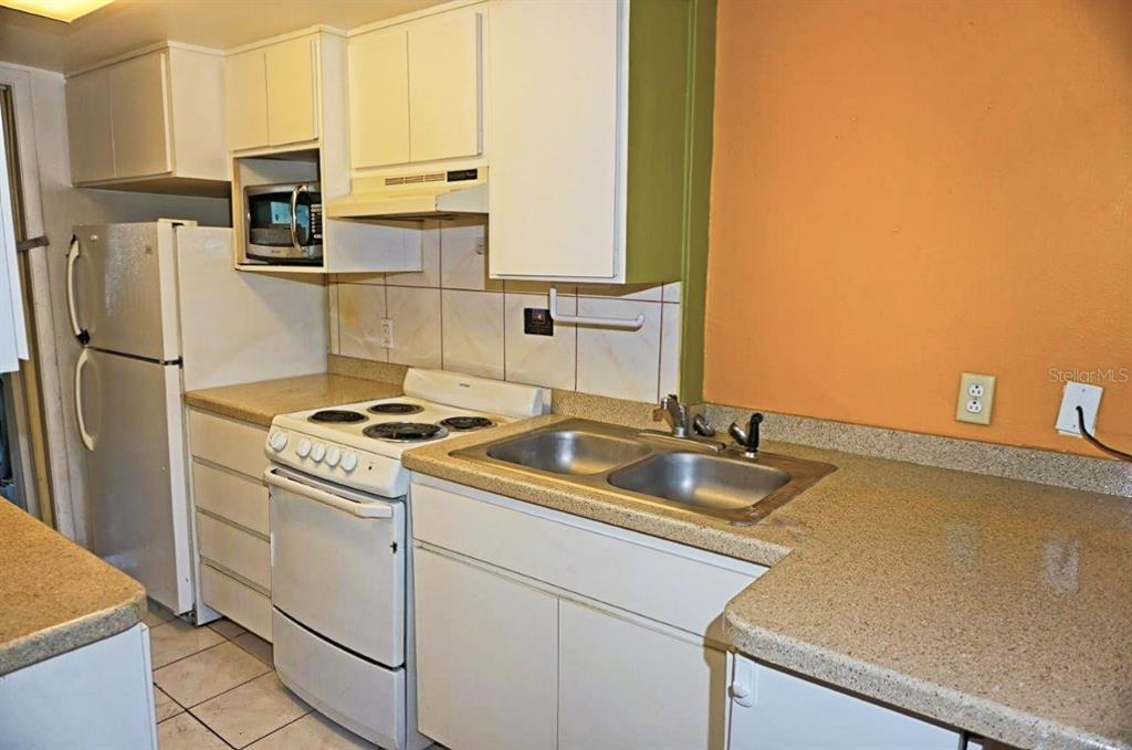 A kitchen features white cabinets, a white stove, a double sink, and orange walls — 1865 MAZO MANOR UNIT J5, LUTZ, FL