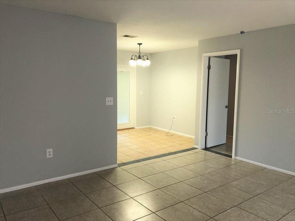 A room with light gray walls and tiled floors leads to a dining area with a chandelier — 700 TRAILWOOD DRIVE, ALTAMONTE SPRINGS, FL