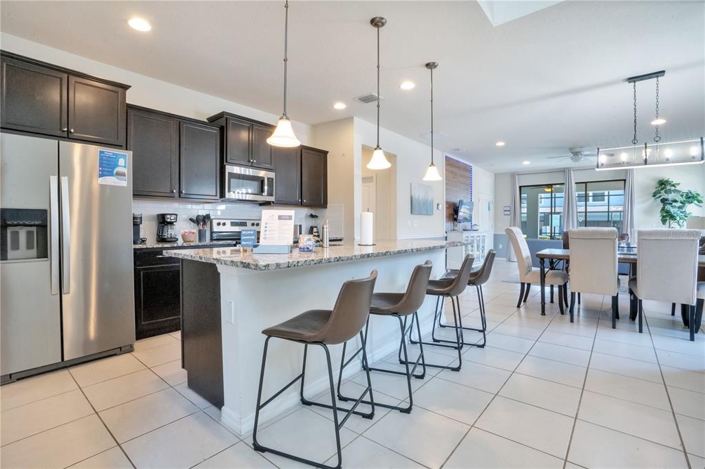 A kitchen features dark cabinets, granite countertops, a breakfast bar with four stools, and tile flooring — 8936 PRAGUE WAY, KISSIMMEE, FL