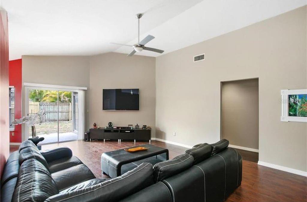 A living room features dark leather sofas, a television, a ceiling fan, and sliding glass doors — 2003 GOLDENDALE COURT, BRANDON, FL