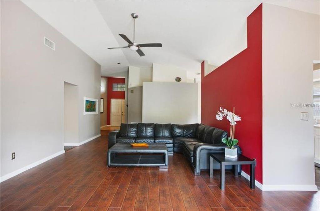 A living room with dark wood floors, a black sectional sofa, and a red accent wall — 2003 GOLDENDALE COURT, BRANDON, FL