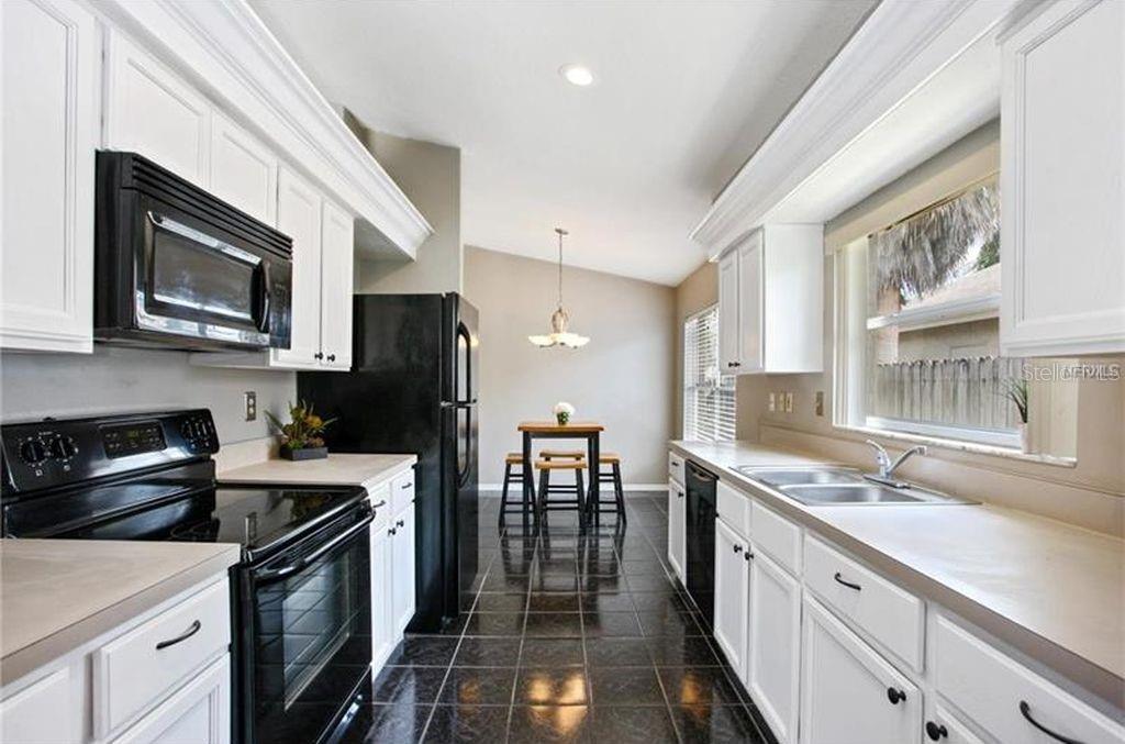 A kitchen with white cabinets, black appliances, and dark tile flooring leads to a dining area — 2003 GOLDENDALE COURT, BRANDON, FL