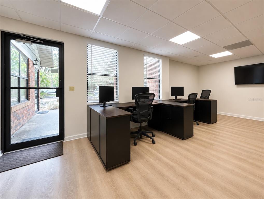 An office room features two L-shaped desks, rolling chairs, light wood flooring, and a glass door — 2731 NW 41ST STREET UNIT B2, GAINESVILLE, FL