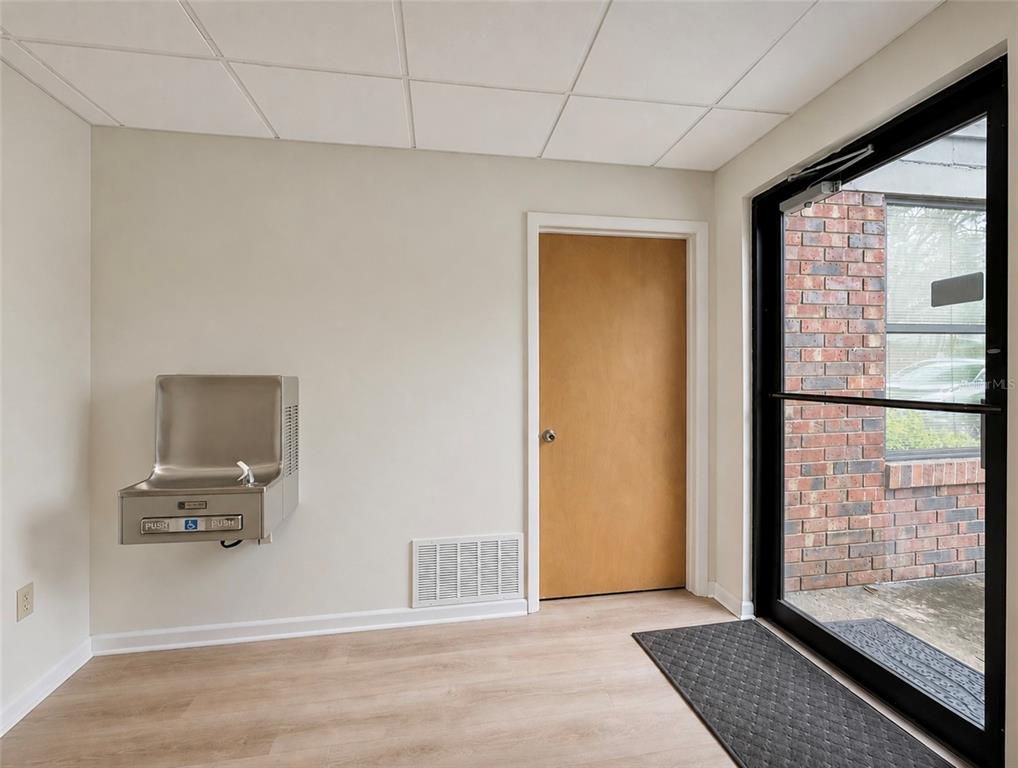 A room with light wood-look flooring, a water fountain, a wooden door, and a glass door — 2731 NW 41ST STREET UNIT B2, GAINESVILLE, FL