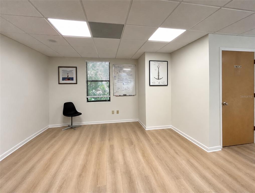 A minimalist office room features light wood-look flooring, a single black chair, and a whiteboard — 2731 NW 41ST STREET UNIT B2, GAINESVILLE, FL