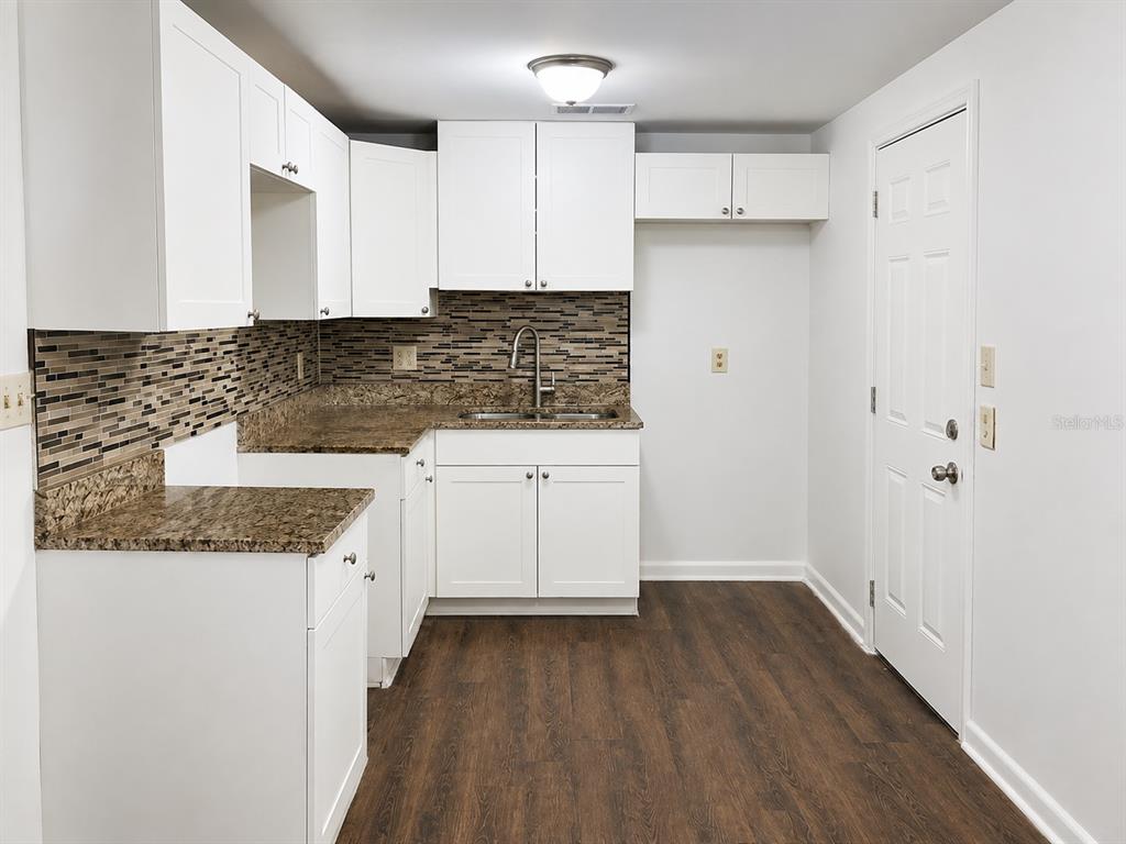 A kitchen with white cabinets, granite countertops, a tiled backsplash, and dark wood-look flooring — 2318 E 111TH AVE, TAMPA, FL
