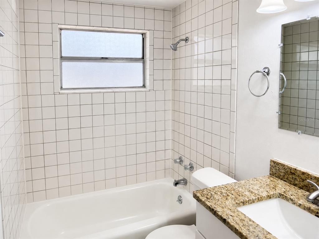 A bathroom features a white tiled shower-tub combination, a granite vanity top, and a wall mirror — 2318 E 111TH AVE, TAMPA, FL