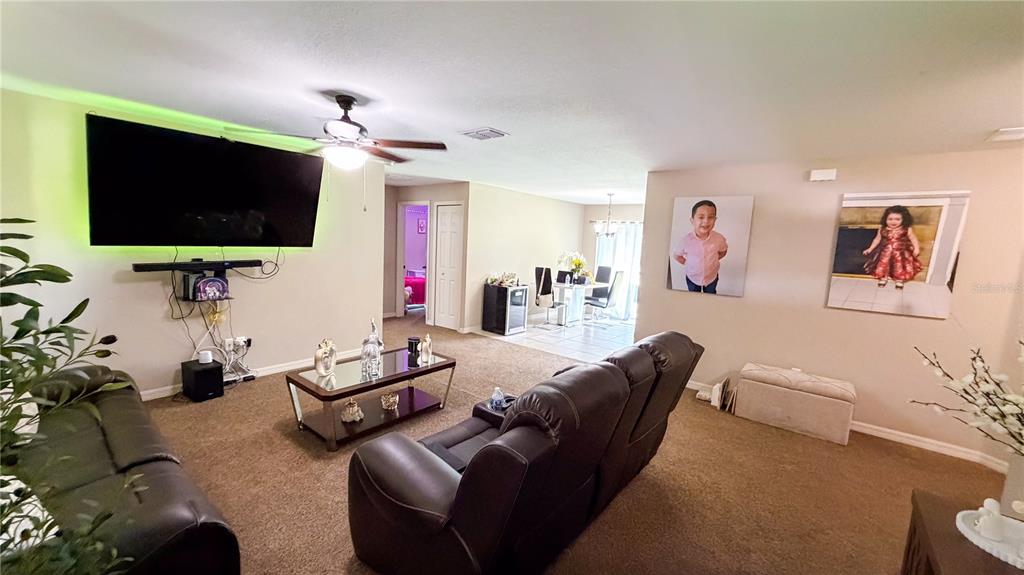 A living room features brown carpet, dark leather furniture, a large television, and wall portraits — 16222 SW 28TH COURT, OCALA, FL