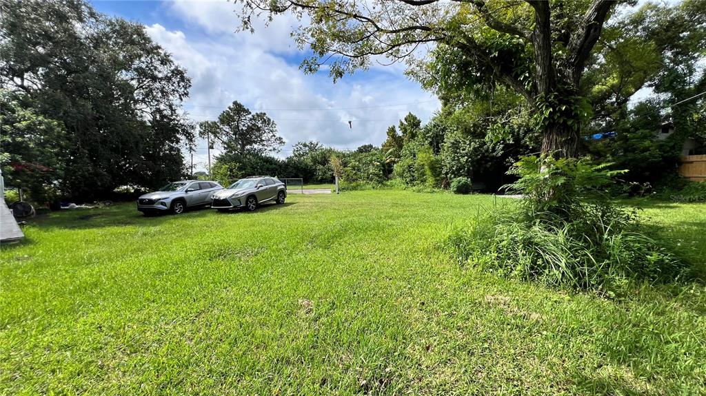 A grassy, open lot features two parked cars and several large trees under a cloudy sky — 730 N COMBEE ROAD, LAKELAND, FL