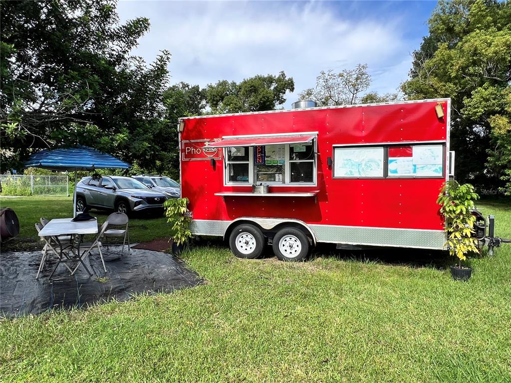 A red food trailer sits on a grassy lot next to an outdoor dining area — 730 N COMBEE ROAD, LAKELAND, FL