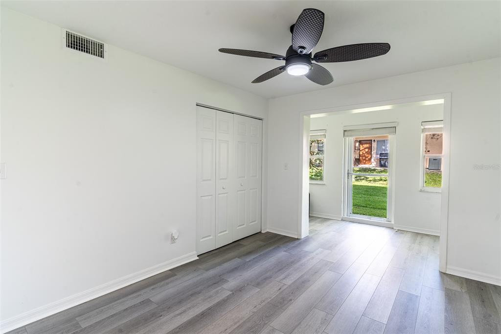 A room with gray wood-look flooring, a ceiling fan, and a doorway to a sunroom — 1100 MARTINIQUE DRIVE UNIT 106, WINTER HAVEN, FL