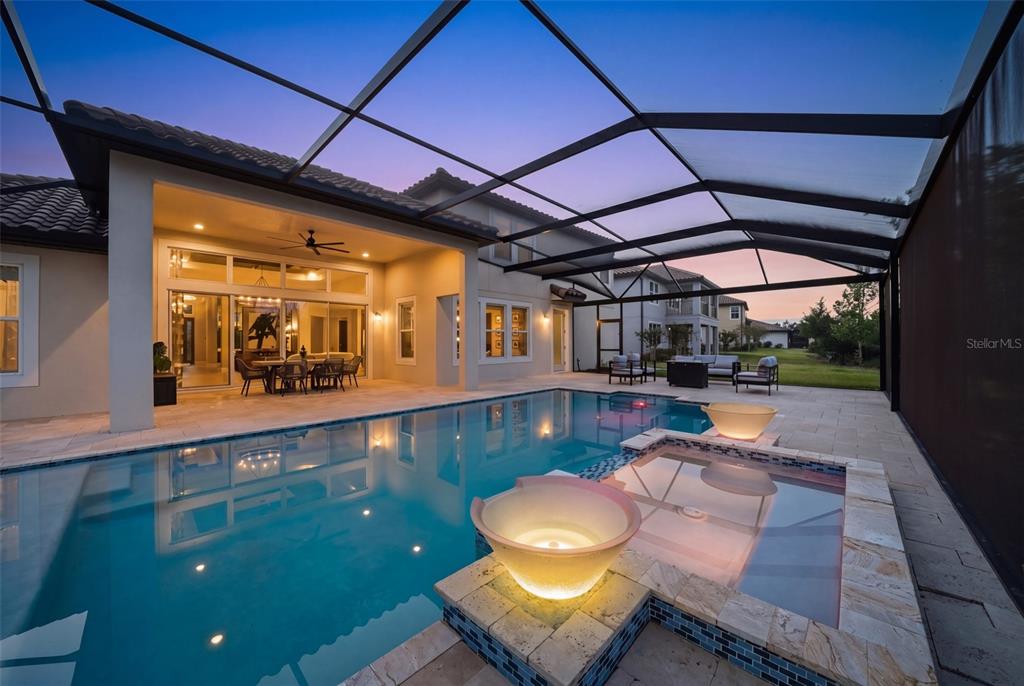 A screened-in patio features a swimming pool, a hot tub, and outdoor seating at dusk — 7224 GRAYBROOK DRIVE, WESLEY CHAPEL, FL
