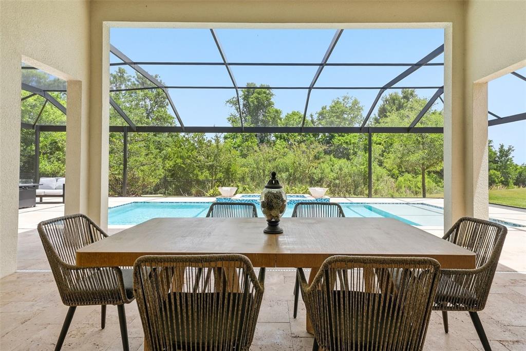 A covered patio features a dining table overlooking a swimming pool and a screened enclosure — 7224 GRAYBROOK DRIVE, WESLEY CHAPEL, FL