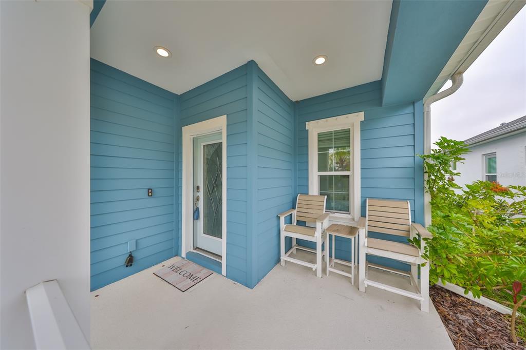 A blue-sided front porch features a white door, two chairs, a small table, and lighting — 11008 SAND PINE LANE, PARRISH, FL