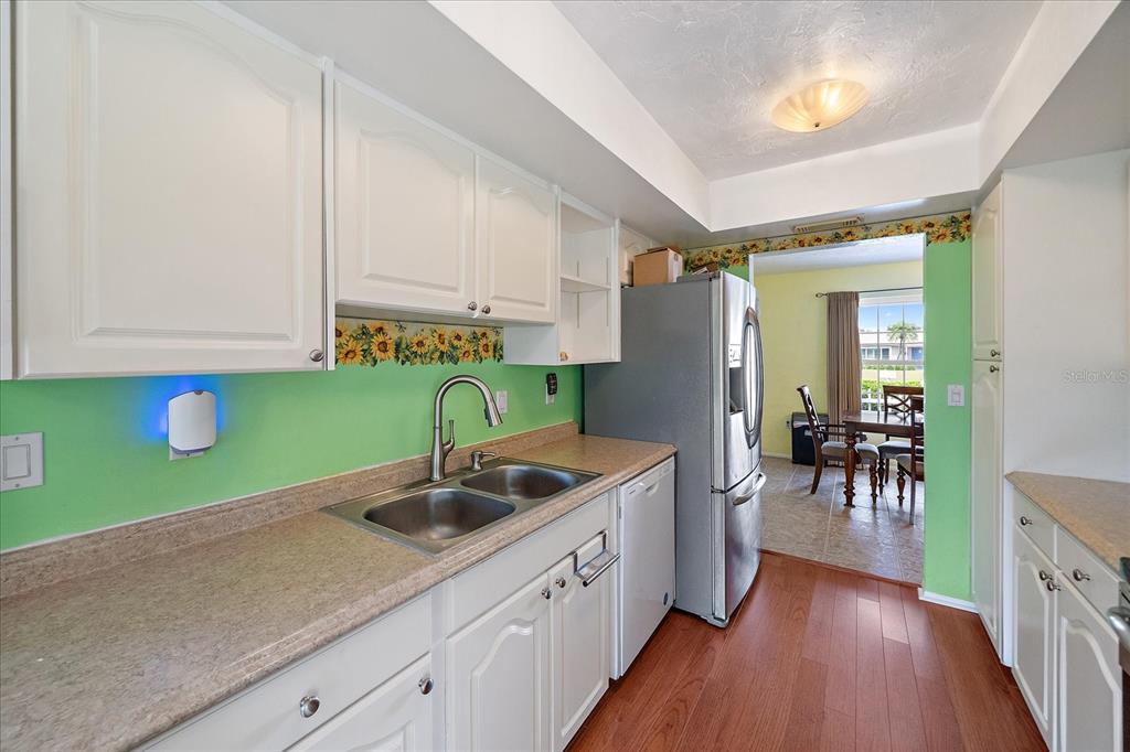 A kitchen features white cabinets, a green backsplash with sunflower trim, and stainless steel appliances — 7403 14TH AVENUE W, BRADENTON, FL