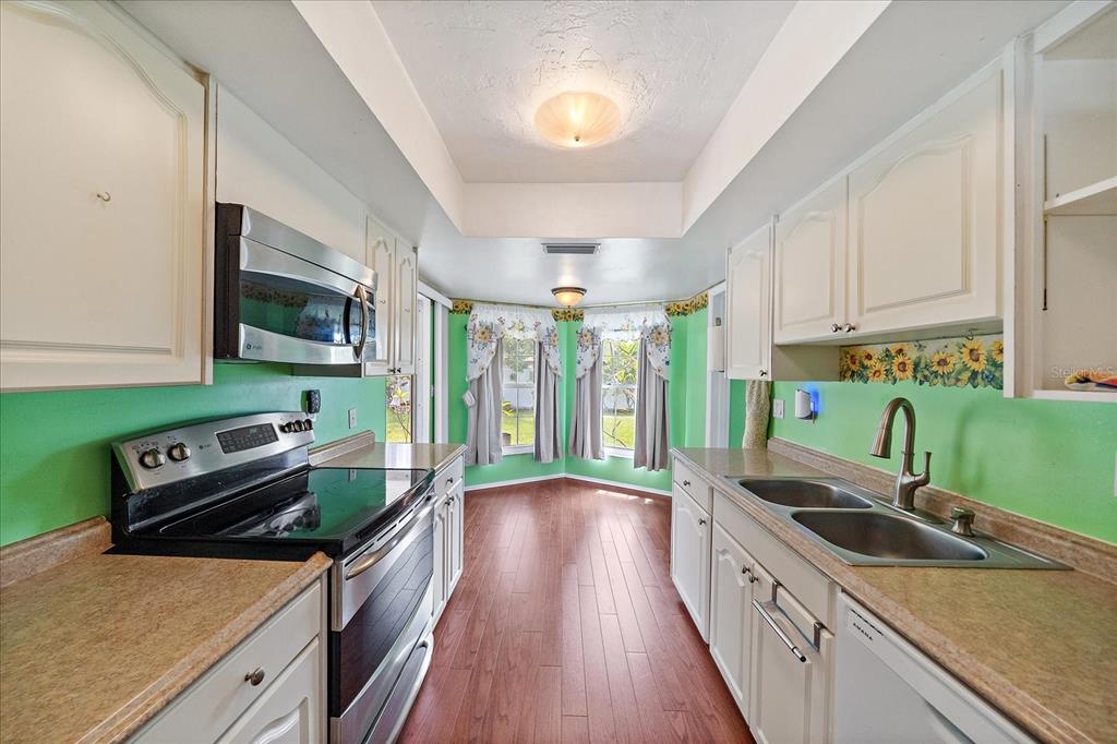 A galley kitchen features white cabinets, green walls, stainless steel appliances, and wood-look flooring — 7403 14TH AVENUE W, BRADENTON, FL