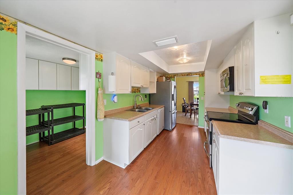 A kitchen with white cabinets, green walls, laminate countertops, and wood-look flooring — 7403 14TH AVENUE W, BRADENTON, FL