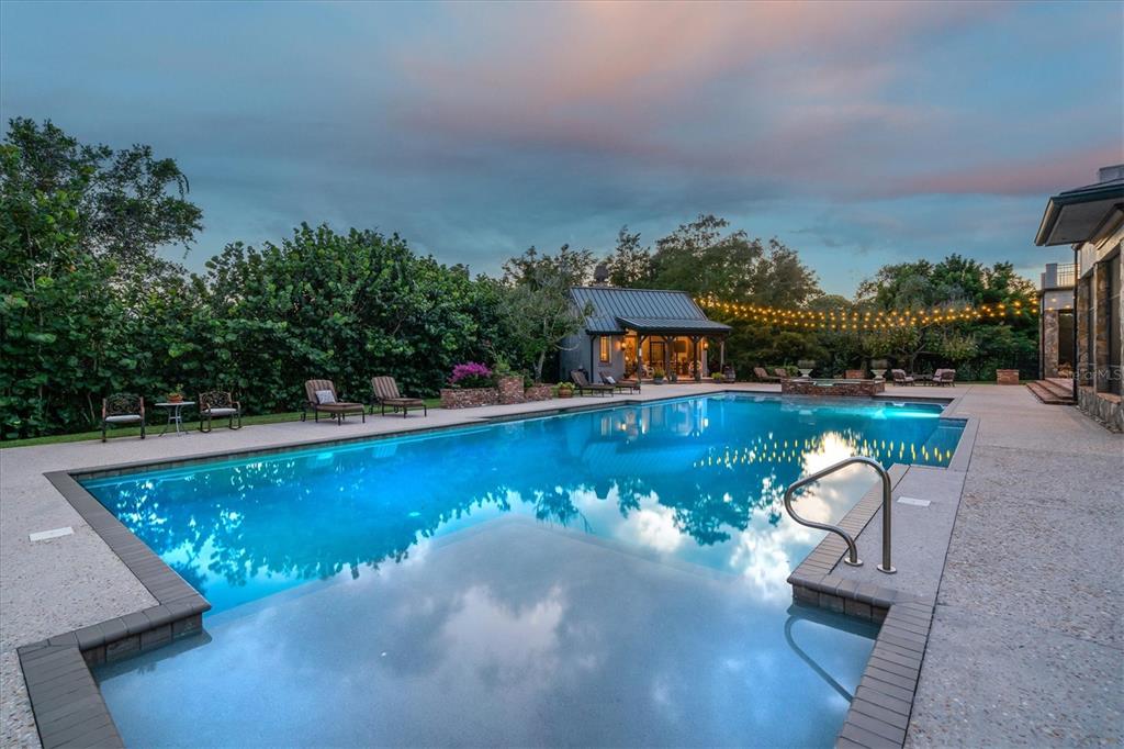 A large swimming pool with a sun shelf sits in a backyard with a pool house — 586 WETHERSFIELD PLACE, MELBOURNE, FL