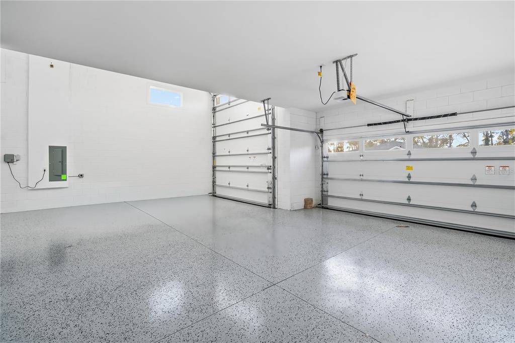 An empty garage with white block walls, a speckled epoxy floor, and two overhead doors — 9120 PLAYERS DRIVE, WEEKI WACHEE, FL