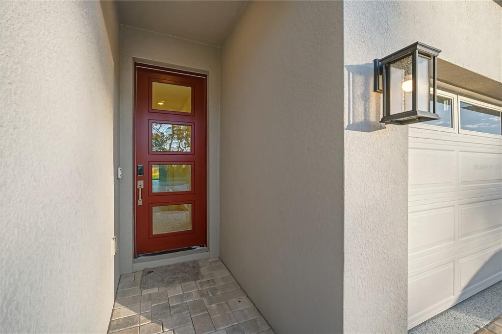 A red front door with four glass panels sits next to a white garage door — 9120 PLAYERS DRIVE, WEEKI WACHEE, FL
