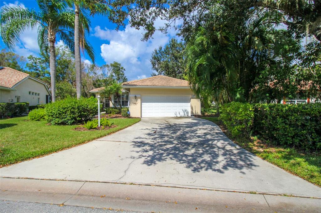 A single-story house with a two-car garage, concrete driveway, and surrounding palm trees and landscaping — 6662 OAKBROOKE CIRCLE, BRADENTON, FL