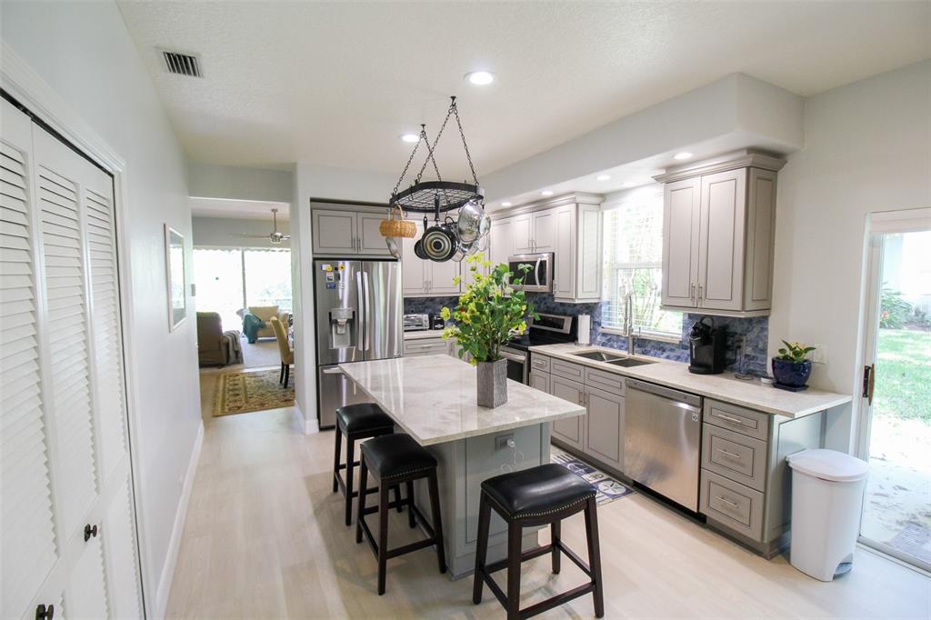 A kitchen with light gray cabinets, a marble-topped island, stainless steel appliances, and tile backsplash — 6662 OAKBROOKE CIRCLE, BRADENTON, FL